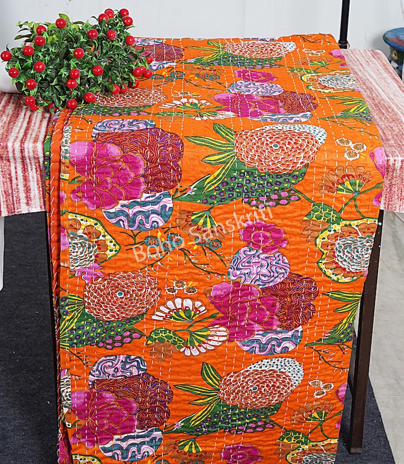 K&ouml;nnte beinhalten: Orangefarbene Kantha-Steppdecke mit einem floralen Muster in Rosa-, Gr&uuml;n- und Lilat&ouml;nen. Die Decke ist aus Baumwolle und hat ein handgesticktes Design.