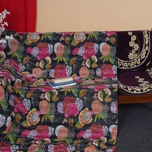 May include: A black kantha quilt with a floral pattern in shades of pink, orange, and green. The quilt is draped over a wooden chair with a purple cushion.
