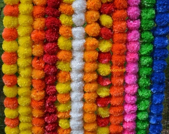 Puede incluir: Una colección de guirnaldas de caléndula de colores, también conocidas como cuerdas de flores, en amarillo, naranja, rojo, blanco, rosa, verde y azul. Las guirnaldas están hechas de caléndulas artificiales y están enhebradas juntas con una cuerda. Las guirnaldas están colgadas en una valla de alambre.