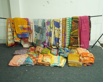 May include: A collection of colorful, patterned quilts and throws. Some are folded, others are hanging on a black bar. The textiles feature various designs, including floral and geometric patterns. The text "Boho Sanskriti" is visible on some of the quilts.