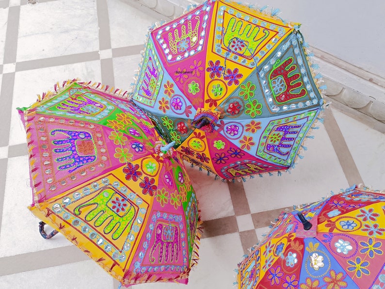 Puede incluir: Tres paraguas coloridos con dise&ntilde;os bordados que representan elefantes, flores y patrones geom&eacute;tricos. Los paraguas est&aacute;n hechos de tela y tienen un estilo tradicional indio.