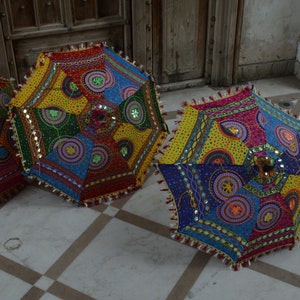 May include: Three colorful, round, fabric umbrellas with intricate patterns and embellishments. The umbrellas are made of patchwork fabric with various colors, including red, blue, yellow, green, and pink. The umbrellas have a fringe trim and are decorated with sequins and beads.