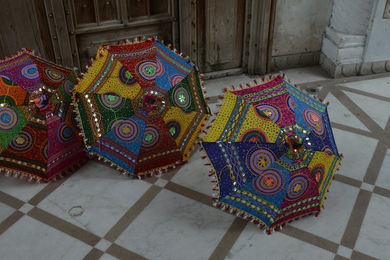May include: Three colorful, round, fabric umbrellas with intricate patterns and embellishments. The umbrellas are made of patchwork fabric with various colors, including red, blue, yellow, green, and pink. The umbrellas have a fringe trim and are decorated with sequins and beads.