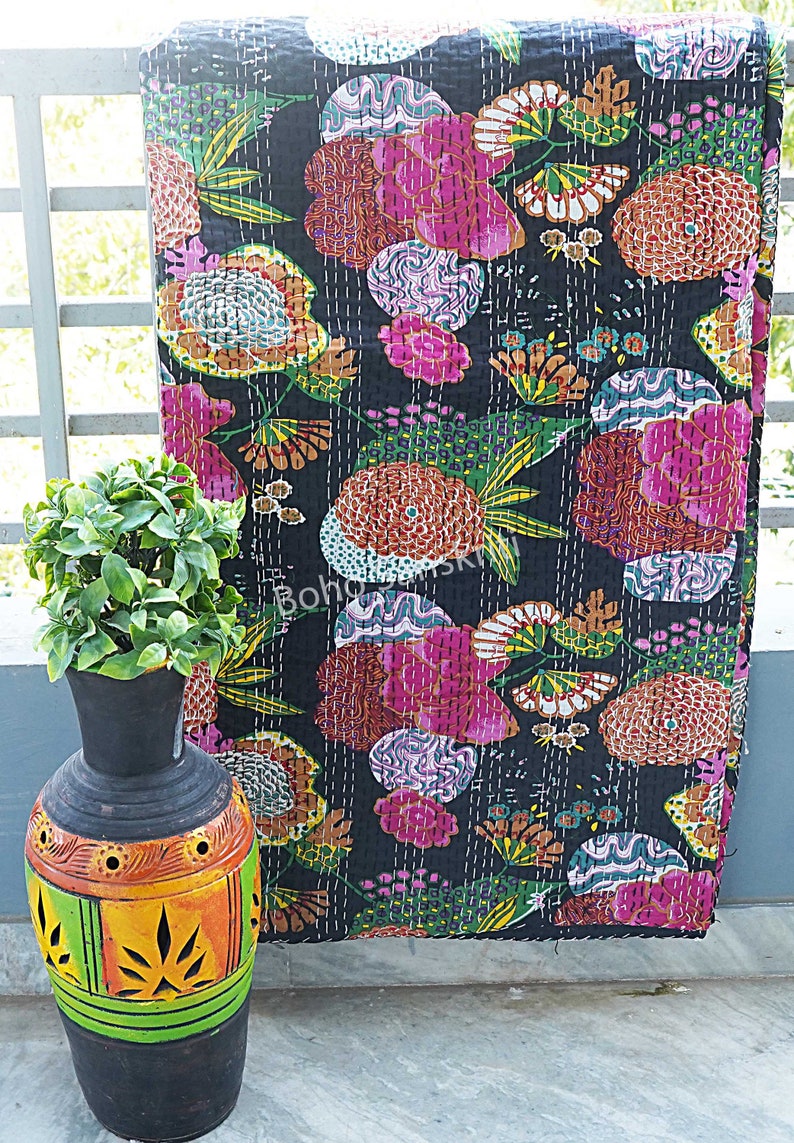 K&ouml;nnte beinhalten: Eine schwarze Kantha-Steppdecke mit einem farbenfrohen Blumenmuster. Die Steppdecke ist aus Baumwolle und hat ein handgesticktes Design. Die Steppdecke ist &uuml;ber einem Gel&auml;nder drapiert, im Vordergrund steht eine dekorative Vase.