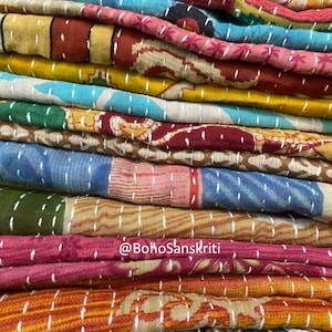 May include: A stack of colourful kantha quilts with white stitching. The quilts are made of various fabrics and patterns. The text "@bohoSanskriti" is visible on the bottom of the stack.