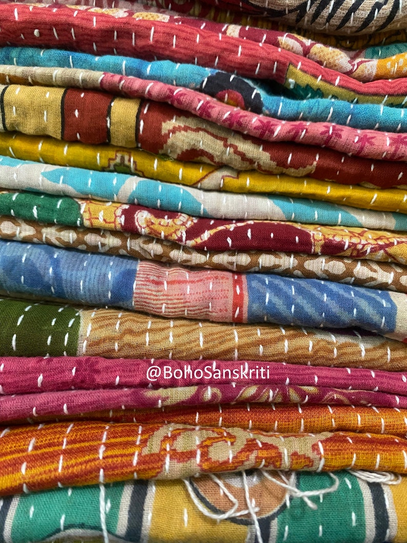 May include: A stack of colourful kantha quilts with white stitching. The quilts are made of various fabrics and patterns. The text "@bohoSanskriti" is visible on the bottom of the stack.
