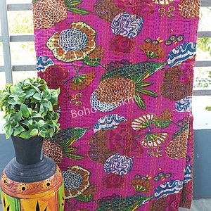 K&ouml;nnte beinhalten: Eine rosafarbene Kantha-Steppdecke mit einem Blumenmuster. Die Decke ist aus Baumwolle und hat ein handgesticktes Design. Die Decke ist gefaltet und auf einem Tisch ausgestellt.