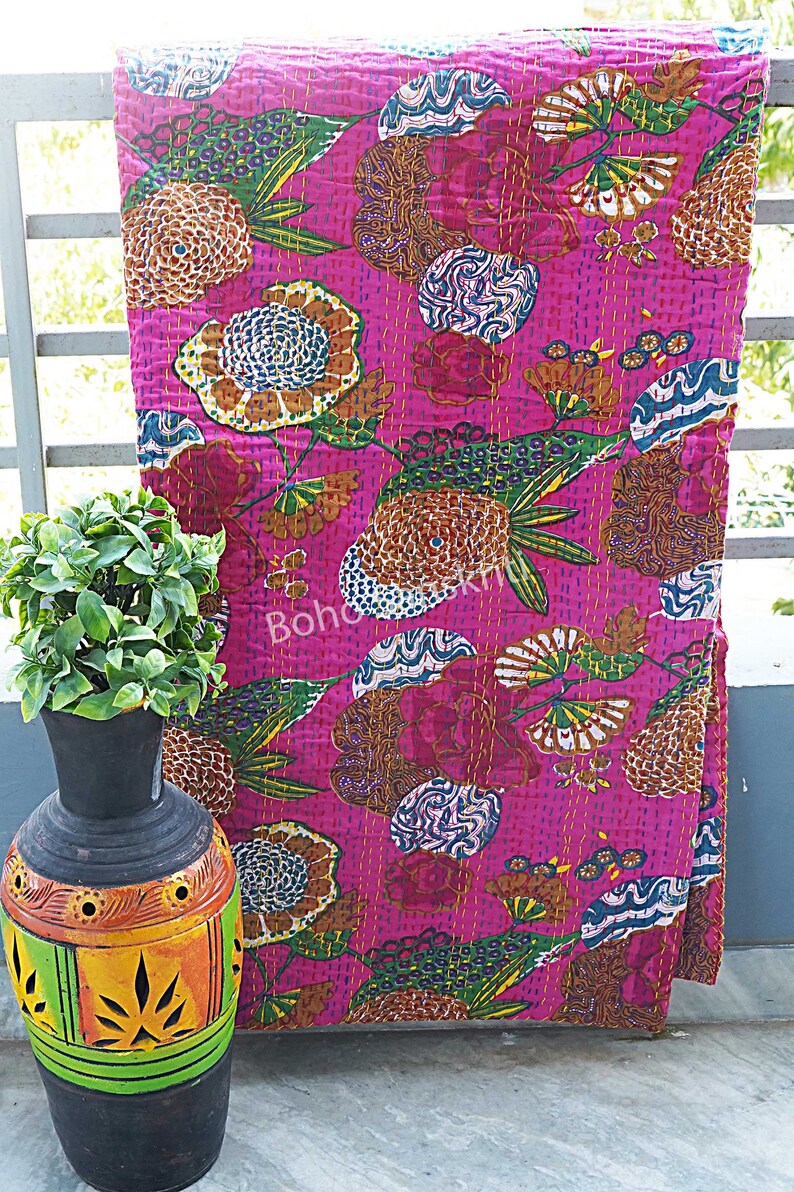 K&ouml;nnte beinhalten: Eine rosafarbene Kantha-Steppdecke mit einem Blumenmuster. Die Decke ist aus Baumwolle und hat ein handgesticktes Design. Die Decke ist gefaltet und auf einem Tisch ausgestellt.