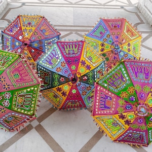 Puede incluir: Cuatro paraguas coloridos con bordados intrincados y lentejuelas. Los paraguas est&aacute;n hechos de tela y tienen un dise&ntilde;o tradicional indio. Est&aacute;n dispuestos en un suelo de baldosas.