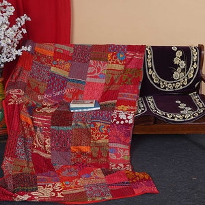 May include: A red, orange, and purple patchwork quilt with a floral pattern. The quilt is folded and draped over a wooden couch with a purple cushion. The text "Boho Sanskriti" is visible on the quilt.