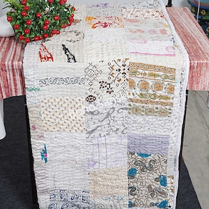 Op de afbeelding: Een wit patchwork-deken met verschillende bloemen- en geometrische patronen. Het deken is gemaakt van gerecyclede sari's en met de hand gestikt.