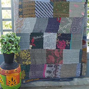 May include: A patchwork quilt made from a variety of fabrics in shades of gray, blue, green, and pink. The quilt is hand-stitched and has a unique, rustic look. The quilt is hanging on a railing and has the text "Boho Sanskrit" printed on it.