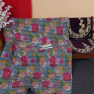 May include: A blue kantha quilt with a floral and pineapple pattern. The quilt is draped over a wooden bench with a purple cushion.