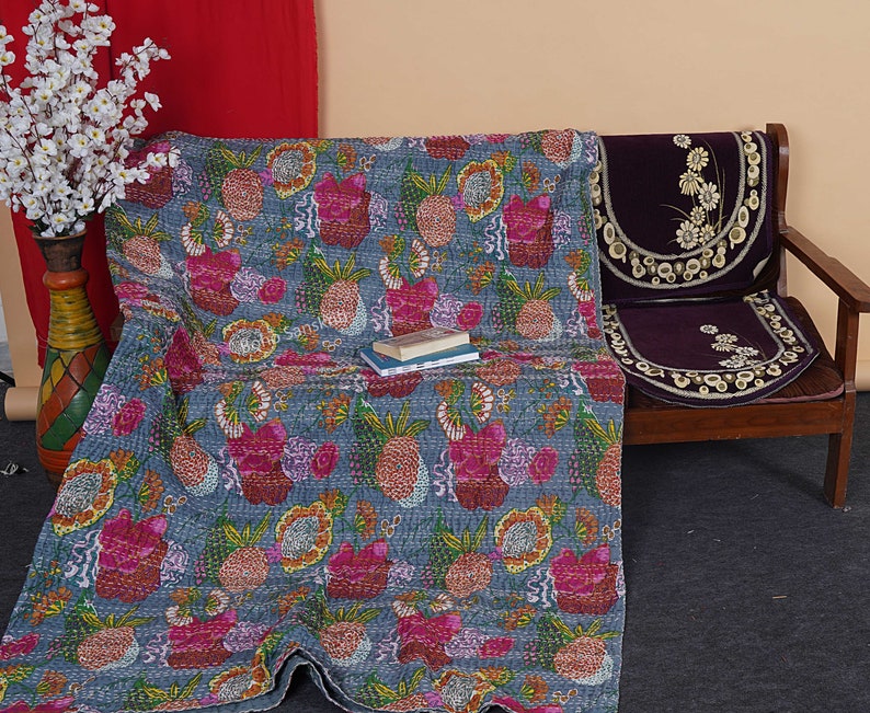 May include: A blue kantha quilt with a floral and pineapple pattern. The quilt is draped over a wooden bench with a purple cushion.