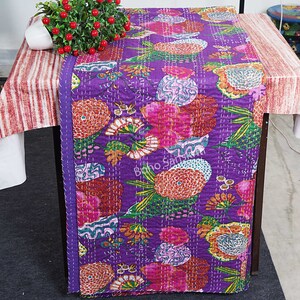 May include: Purple kantha quilt featuring a floral design in shades of pink, orange, and green. The quilt is hand-stitched and has a fringed edge.