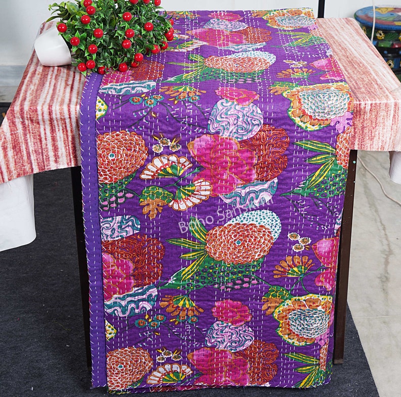 May include: Purple kantha quilt featuring a floral design in shades of pink, orange, and green. The quilt is hand-stitched and has a fringed edge.
