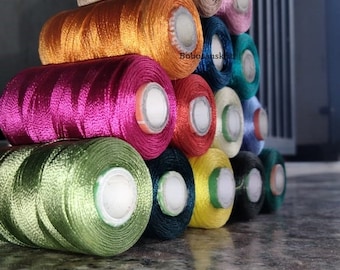 May include: A stack of colorful spools of thread, arranged in a pyramid shape. The spools are made of different materials, including cotton, silk, and polyester. The colors of the thread include blue, brown, orange, pink, green, yellow, and red.