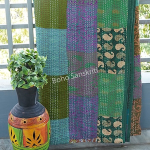 May include: A patchwork quilt with a variety of green, teal, and purple fabric squares. The quilt is hand-stitched with white thread. The text "Boho Sanskriti" is visible on the quilt. A decorative vase with a plant is in the foreground.