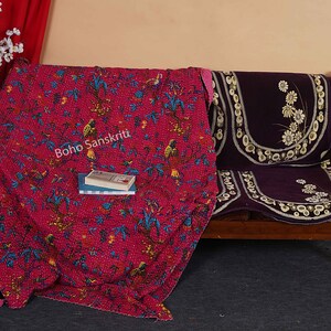 May include: A pink kantha quilt with a floral and bird pattern, draped over a wooden bench with a purple cushion. The quilt has the text "Boho Sanskriti" printed on it.