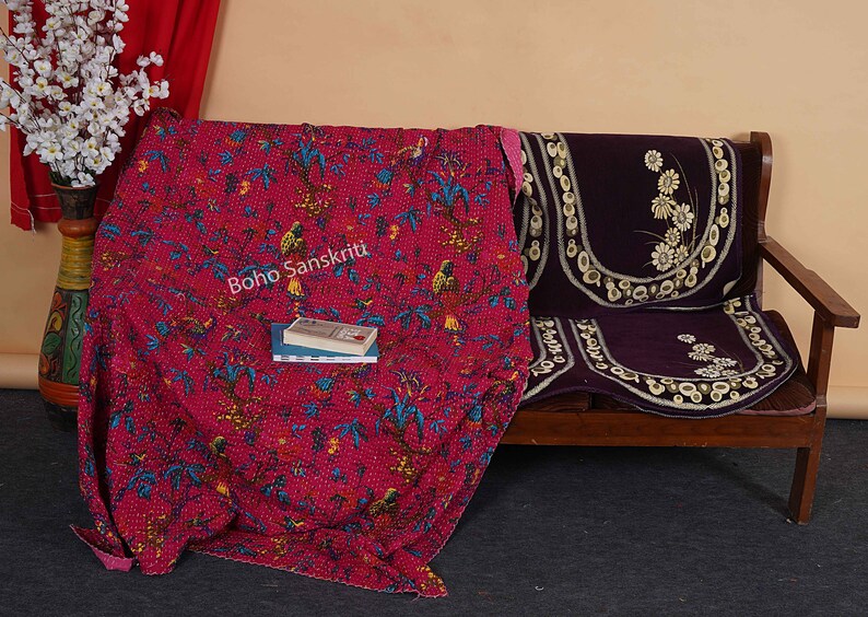 May include: A pink kantha quilt with a floral and bird pattern, draped over a wooden bench with a purple cushion. The quilt has the text "Boho Sanskriti" printed on it.