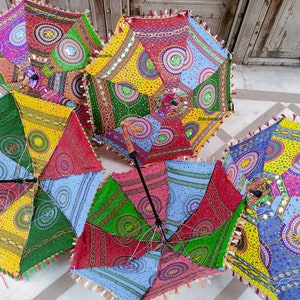 May include: Five colorful, patterned umbrellas with fringe trim. Each umbrella has a different design with circles, dots, and geometric shapes. The umbrellas are made of fabric and have wooden handles.