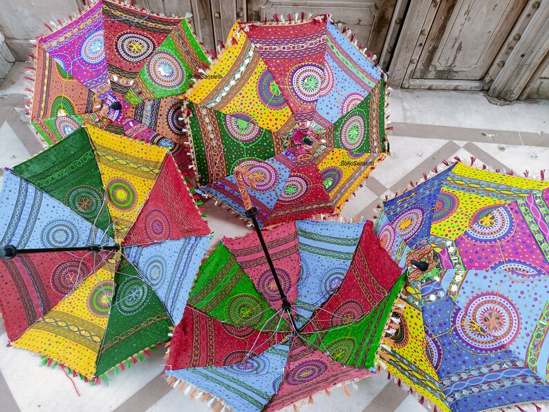 May include: Five colorful, patterned umbrellas with fringe trim. Each umbrella has a different design with circles, dots, and geometric shapes. The umbrellas are made of fabric and have wooden handles.