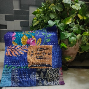 May include: A patchwork pillow with a variety of blue fabrics, floral patterns, and decorative stitching. The pillow has a rectangular shape and features a central patch with the text "BohoSanskriti".