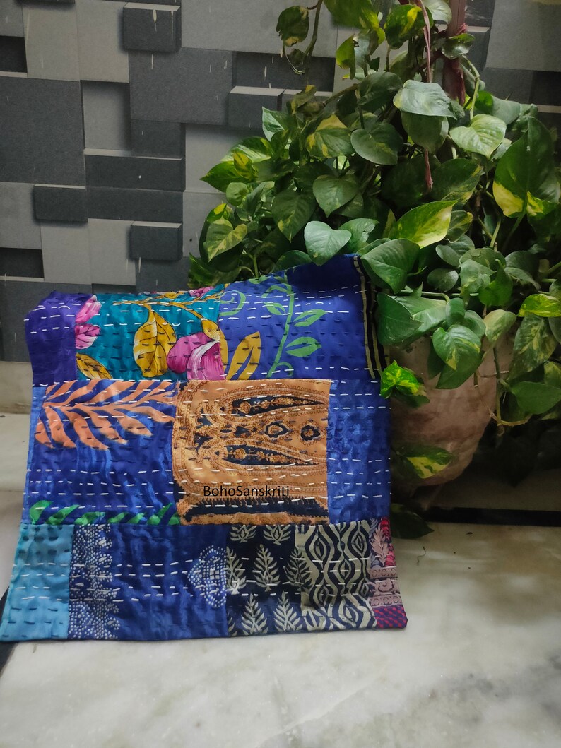 May include: A patchwork pillow with a variety of blue fabrics, floral patterns, and decorative stitching. The pillow has a rectangular shape and features a central patch with the text "BohoSanskriti".