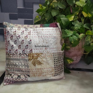 May include: Square patchwork pillow with a variety of patterned fabrics in cream, burgundy, and black. The pillow features visible stitching and the text "BohoSanskriti". A potted plant is in the background.