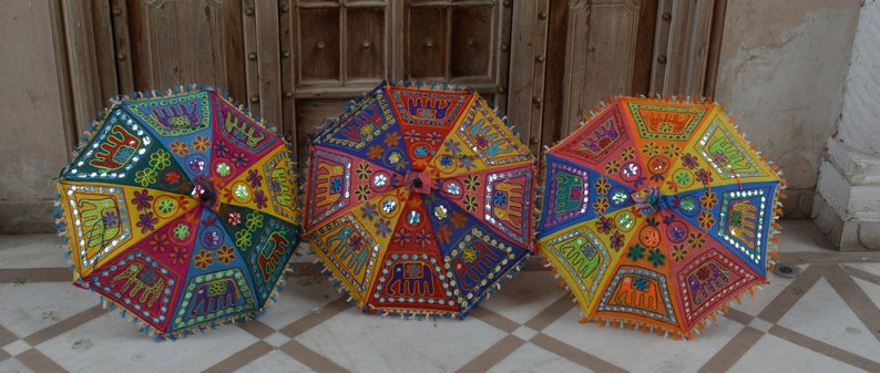 Puede incluir: Tres sombrillas coloridas con bordados intrincados y adornos de espejo. Las sombrillas est&aacute;n hechas de tela y tienen un dise&ntilde;o tradicional indio.