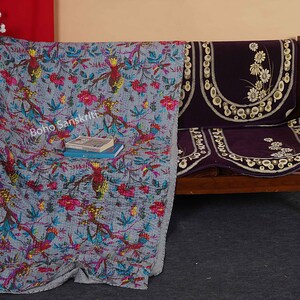 May include: A gray and blue kantha quilt with a floral and bird pattern. The quilt is draped over a wooden bench with a purple cushion. The text "boho sanskriti" is visible on the quilt.