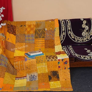 May include: A yellow and orange kantha quilt with a patchwork design. The quilt is draped over a wooden bench with purple cushions. The text "boho sanskriti" is visible on the quilt.