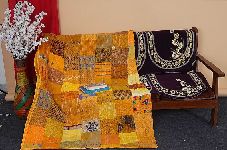 May include: A yellow and orange kantha quilt with a patchwork design. The quilt is draped over a wooden bench with purple cushions. The text "boho sanskriti" is visible on the quilt.