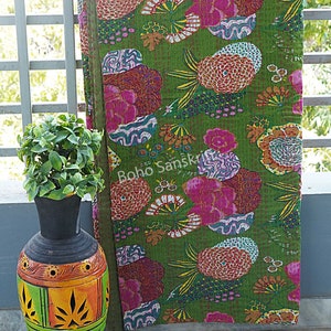 K&ouml;nnte beinhalten: Eine gr&uuml;ne Kantha-Steppdecke mit einem floralen Muster in Rosa-, Orange- und Wei&szlig;t&ouml;nen. Die Steppdecke ist gefaltet und lehnt an einem wei&szlig;en Gel&auml;nder. Der Text "Boho Sanskriti" ist in der linken unteren Ecke des Bildes sichtbar.