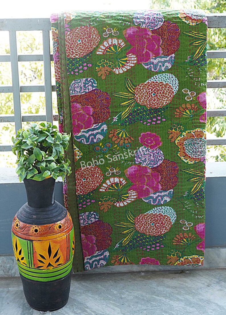 K&ouml;nnte beinhalten: Eine gr&uuml;ne Kantha-Steppdecke mit einem floralen Muster in Rosa-, Orange- und Wei&szlig;t&ouml;nen. Die Steppdecke ist gefaltet und lehnt an einem wei&szlig;en Gel&auml;nder. Der Text "Boho Sanskriti" ist in der linken unteren Ecke des Bildes sichtbar.