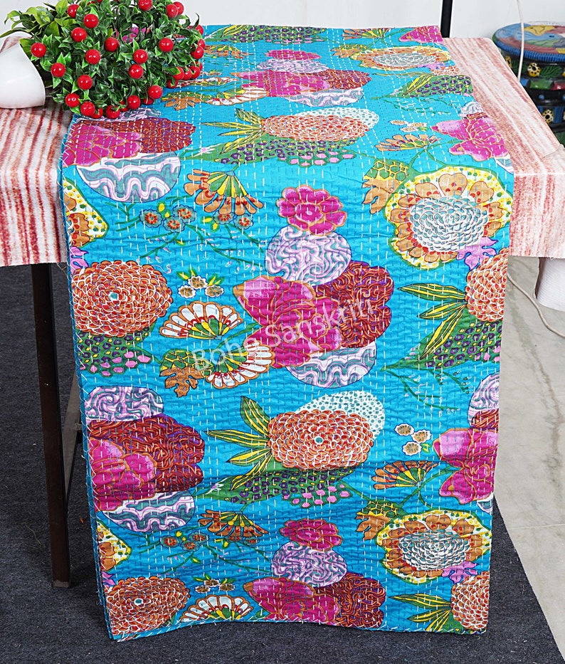 May include: A turquoise blue table runner with a floral pattern. The flowers are in shades of pink, orange, yellow, and green. The runner is quilted and has a subtle sheen.