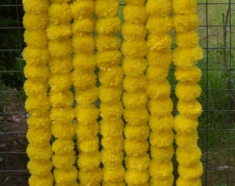 Puede incluir: Un conjunto de 6 guirnaldas de flores de caléndula amarillas, cada guirnalda mide aproximadamente 90 cm de largo. Las guirnaldas están hechas de caléndulas artificiales y son perfectas para decorar bodas, festivales u otras ocasiones especiales. Las guirnaldas están colgadas en una valla metálica. El texto "bohoSanskruti" es visible en las guirnaldas.