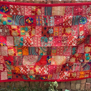 May include: A patchwork textile with a red border. The textile is composed of numerous squares in shades of red, orange, and gold, with embroidered and patterned details. The text "BohoSanskruti" is visible in the upper left corner.