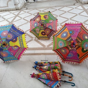 May include: Three colorful, patterned umbrellas with fringe trim and sequins. The umbrellas are laid out on a white tiled floor.