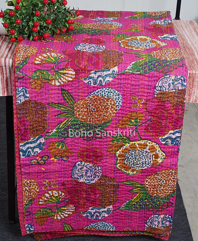 May include: A pink kantha quilt with a floral pattern in shades of brown, green, and blue. The quilt is made of cotton and has a hand-stitched design.