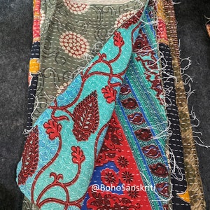 May include: A multi-coloured kantha quilt featuring a variety of floral patterns. The quilt is made from recycled saris and is hand-stitched. The quilt is folded in half, showcasing the stitching. The quilt is made by @bohoSanskruti.