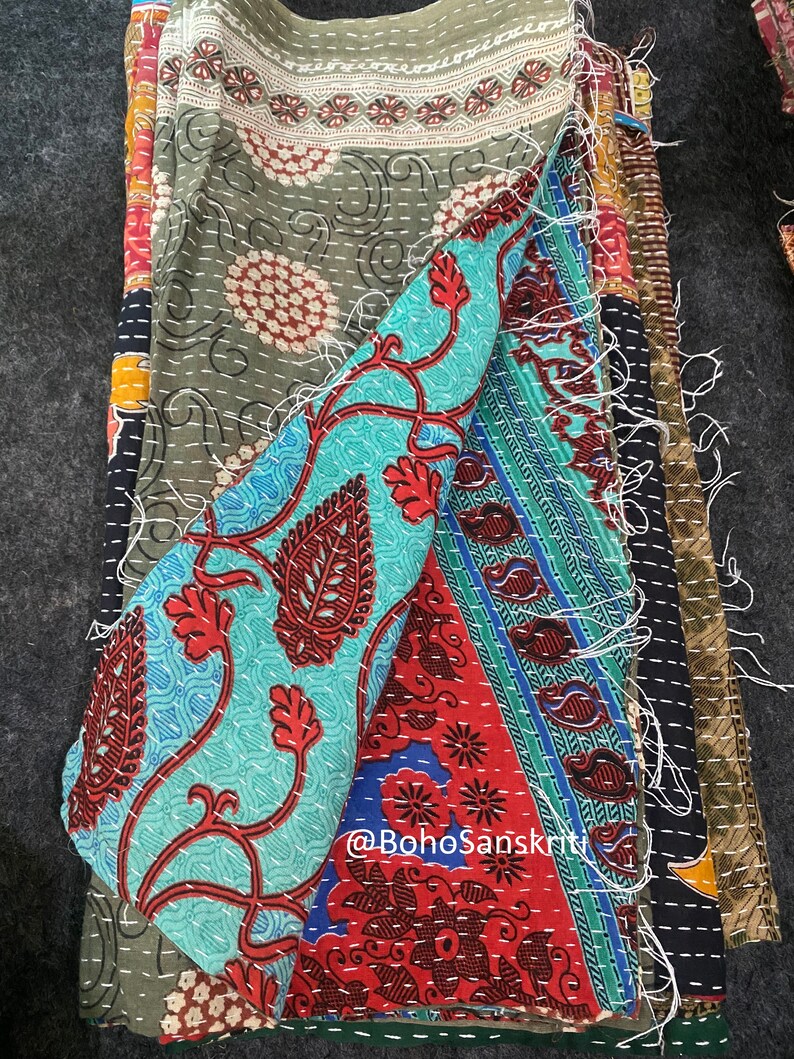 May include: A multi-coloured kantha quilt featuring a variety of floral patterns. The quilt is made from recycled saris and is hand-stitched. The quilt is folded in half, showcasing the stitching. The quilt is made by @bohoSanskruti.