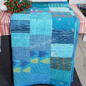 May include: A patchwork quilt made from repurposed silk saris in shades of blue, green, and gold. The quilt is hand-stitched and has a unique, textured look.