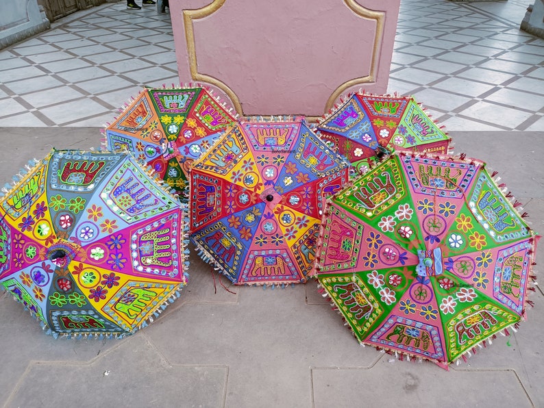 Puede incluir: Una colecci&oacute;n de cinco paraguas coloridos con bordados e incrustaciones intrincados. Los paraguas est&aacute;n hechos de tela y tienen una variedad de patrones, incluyendo dise&ntilde;os florales, formas geom&eacute;tricas y motivos de animales. Los paraguas est&aacute;n dispuestos en semic&iacute;rculo sobre un suelo de baldosas.