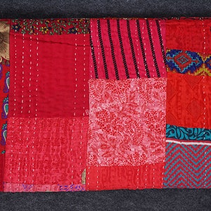May include: A red patchwork quilt featuring a variety of patterns and colours, including paisley, floral, and geometric designs. The quilt is crafted from recycled saris and is hand-stitched.