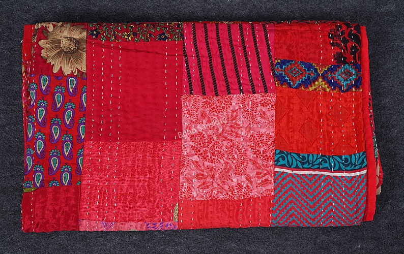 May include: A red patchwork quilt featuring a variety of patterns and colours, including paisley, floral, and geometric designs. The quilt is crafted from recycled saris and is hand-stitched.