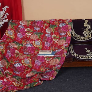 May include: A red floral kantha quilt with a multi-colored floral pattern. The quilt is draped over a wooden bench with purple cushions. The text "Boho Sanskrit" is visible on the quilt.