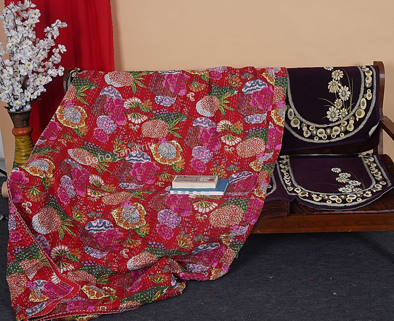 May include: A red floral kantha quilt with a multi-colored floral pattern. The quilt is draped over a wooden bench with purple cushions. The text "Boho Sanskrit" is visible on the quilt.