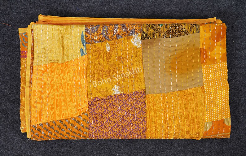 May include: A patchwork quilt made of various shades of yellow and orange fabric. The quilt is hand-stitched and has a unique, rustic look. "Boho Sanskriti" is printed on the quilt.