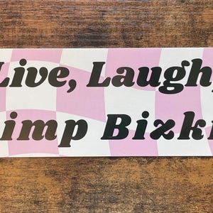 May include: A pink and white checkered sticker with the text "Live, Laugh, Limp Bizkit" in black.